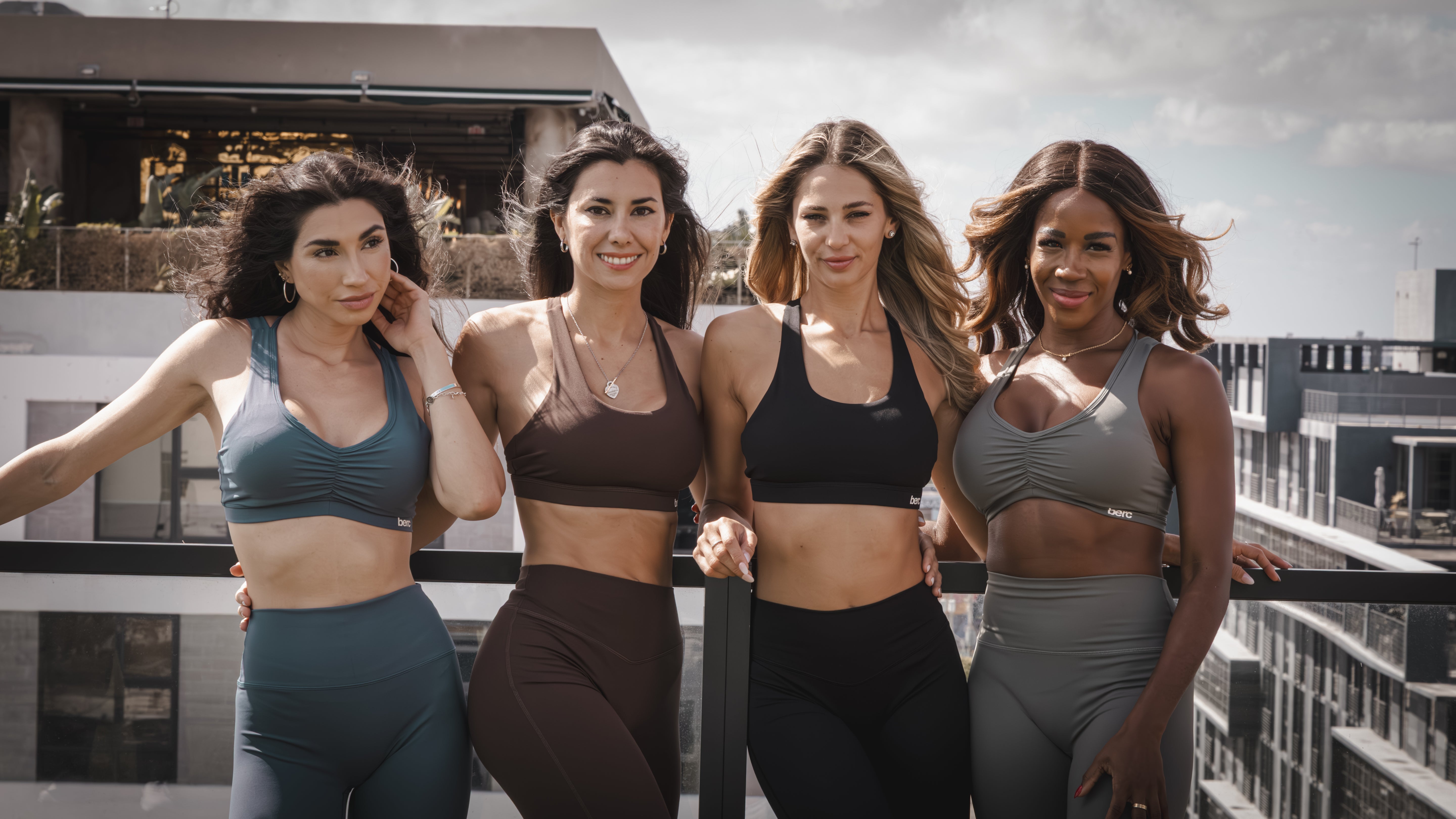 Four women in athletic wear standing together on a rooftop with cityscape background